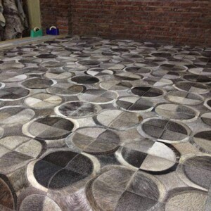 May include: A gray and white patterned rug made of cowhide. The rug is made up of circles and squares.