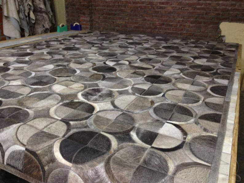 May include: A gray and white patterned rug made of cowhide. The rug is made up of circles and squares.