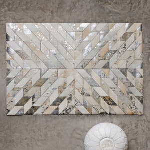 May include: A white and silver geometric patterned rug made of leather. The rug has a starburst design and is made of small, individual pieces of leather.