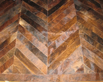 May include: A brown and black chevron patterned cowhide rug. The rug is made of leather and has a natural, rustic look.