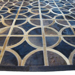 May include: A geometric patterned rug made of leather in shades of brown and blue. The rug is made of individual pieces of leather sewn together to create a circular pattern.