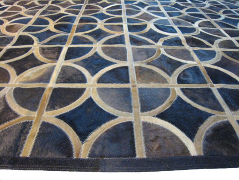 May include: A geometric patterned rug made of leather in shades of brown and blue. The rug is made of individual pieces of leather sewn together to create a circular pattern.