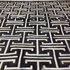 May include: Black and white cowhide rug with a geometric pattern. The rug has a Greek key design.