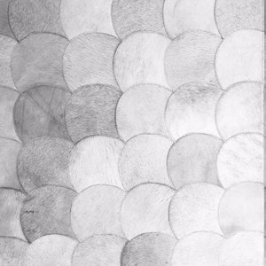 May include: A close-up view of a rug with a pattern of overlapping, semi-circular shapes. The rug is made of a light-colored material, possibly hide or fur, with varying shades of gray and white. The shapes are stitched together.
