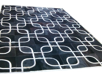 Può includere: Tappeto in pelle di mucca nero e bianco con un motivo geometrico. Il tappeto è realizzato con pezzi di pelle cuciti insieme per creare un design unico.