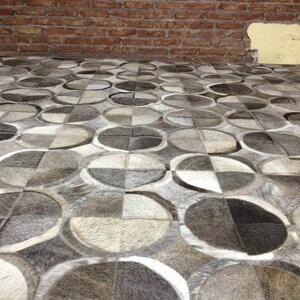 May include: A close-up of a gray and white patterned rug made of cowhide. The rug is made up of many different shapes and sizes of cowhide patches, creating a unique and interesting design.