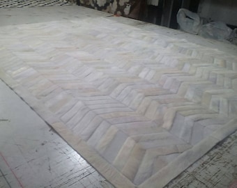 May include: White cowhide rug with a herringbone pattern. The rug is made of natural leather and has a soft, luxurious feel.