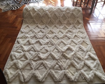 May include: White fluffy rug with a diamond pattern. The rug is rolled up at one end.