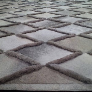 Puede incluir: Una alfombra gris y blanca con estampado de rombos hecha de piel suave y esponjosa.
