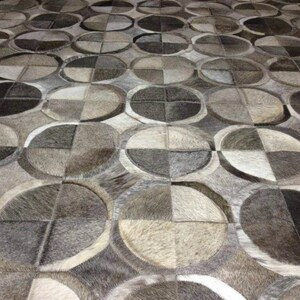 May include: A close-up of a gray and white patterned rug made of cowhide. The rug is made up of many small squares and rectangles, creating a geometric design.