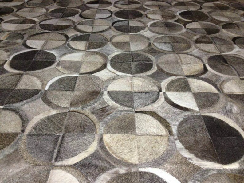 May include: A close-up of a gray and white patterned rug made of cowhide. The rug is made up of many small squares and rectangles, creating a geometric design.