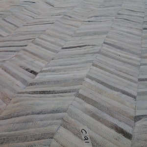 May include: White leather rug with a herringbone pattern. The rug is made of strips of leather sewn together to create a geometric design.