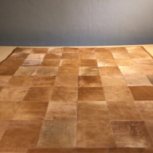 May include: A brown leather patchwork rug with a checkered pattern. The rug is made of squares of different shades of brown leather.