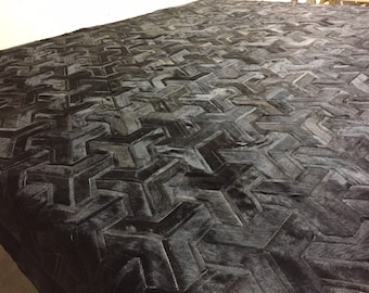 May include: Black and gray cowhide rug with a geometric pattern of arrows. The rug is made of soft, durable leather and has a unique, modern design.