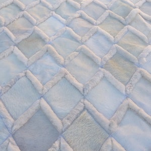 May include: White faux fur rug with a diamond pattern. The rug is made of individual squares of fur sewn together to create a geometric design.