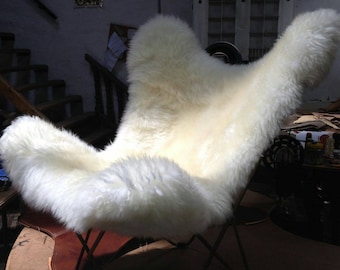 May include: A white sheepskin covered butterfly chair with a metal frame. The chair is in a workshop setting.