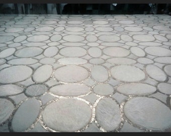 May include: A rug featuring a repeating pattern of off-white, oval-shaped patches arranged in a grid. The individual patches are separated by thin, metallic silver-toned borders that create a geometric network across the entire surface area.