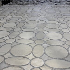 May include: A close-up of a gray and white patterned floor made of small, round stones. The stones are arranged in a repeating pattern of circles and ovals.