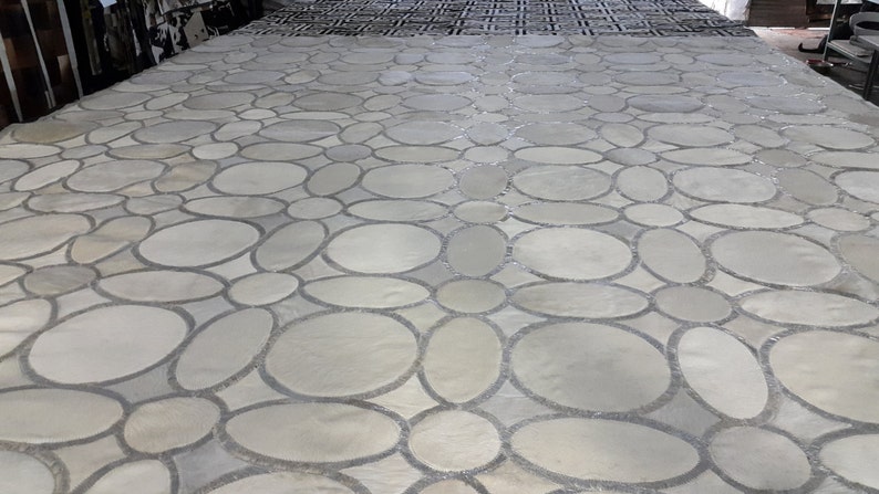 May include: A close-up of a gray and white patterned floor made of small, round stones. The stones are arranged in a repeating pattern of circles and ovals.