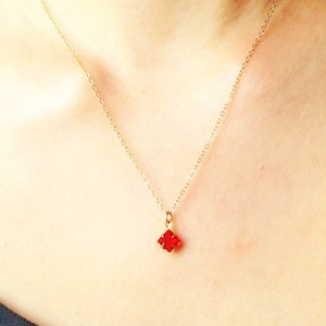 Puede incluir: Un collar de cadena dorada con un pequeño colgante cuadrado rojo.