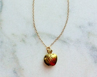 Puede incluir: Un collar de cadena dorada con un pequeño colgante de manzana dorada.