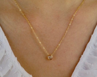 May include: A delicate gold chain necklace with a small, clear gemstone pendant.