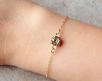 May include: A delicate gold chain bracelet with a single, round, clear crystal charm.