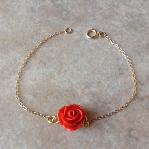 May include: A delicate gold chain bracelet with a single red rose charm.