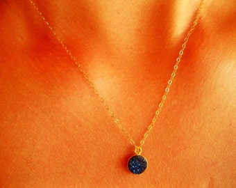 May include: A gold chain necklace with a dark blue, round pendant. The pendant is made of a sparkly material.