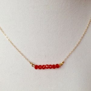 May include: A gold chain necklace with a row of small, red, faceted beads.