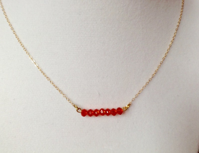 May include: A gold chain necklace with a row of small, red, faceted beads.
