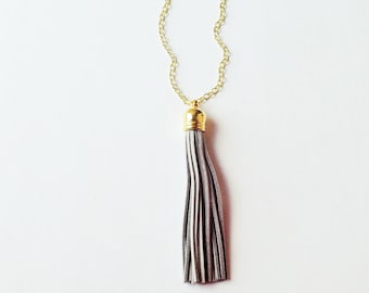 Puede incluir: Un collar de cadena dorada con un colgante de borla de gamuza gris.