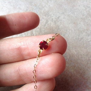 May include: A delicate gold chain necklace with a single red gemstone pendant.