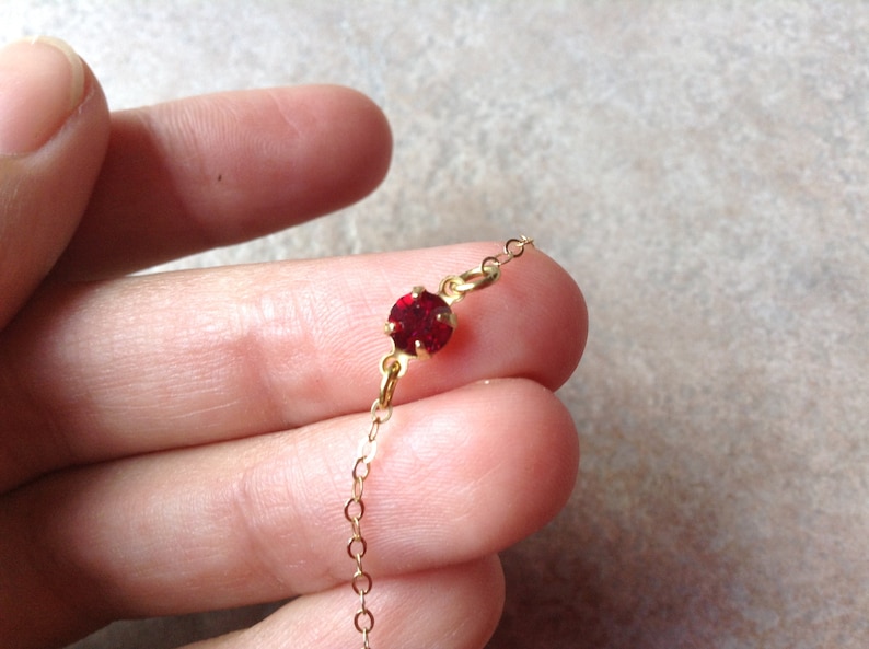 May include: A delicate gold chain necklace with a single red gemstone pendant.