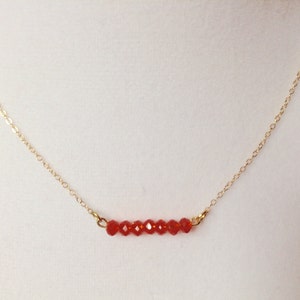 May include: A delicate gold chain necklace with a row of small, red faceted beads.