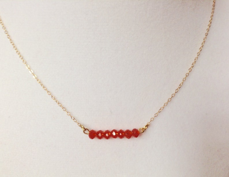 May include: A delicate gold chain necklace with a row of small, red faceted beads.