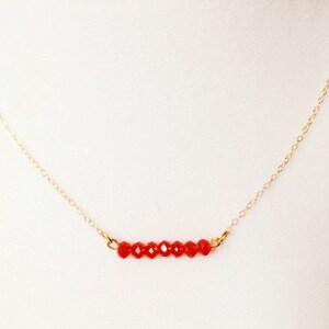 May include: A delicate gold chain necklace with a row of small, red crystal beads.