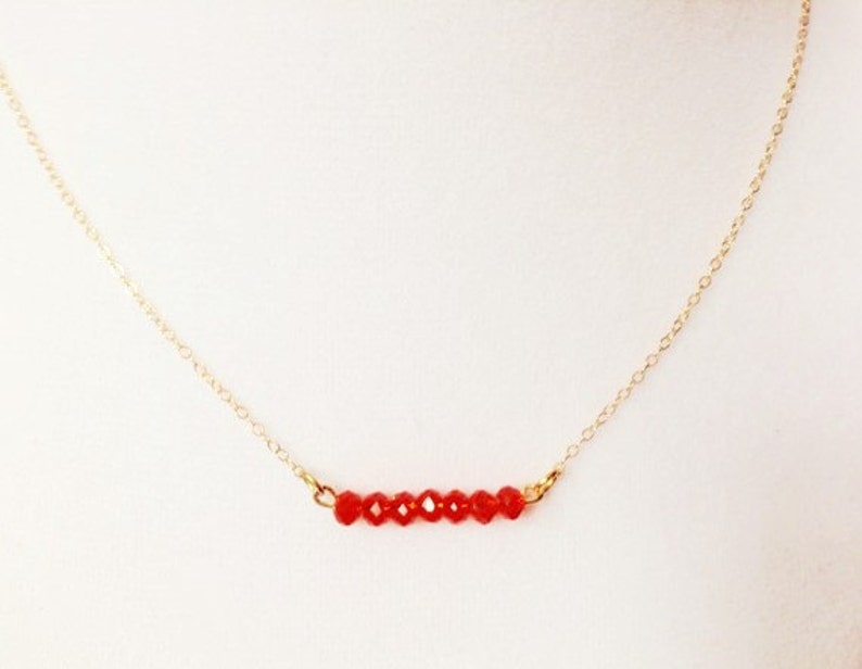 May include: A delicate gold chain necklace with a row of small, red crystal beads.