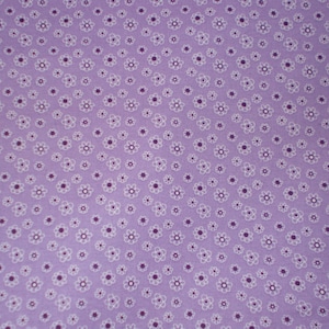 May include: A light purple fabric featuring a repeating pattern of small white outlined flowers with dark purple centers. The floral design is evenly spaced across the entire surface of the textile, creating a consistent and uniform visual texture.