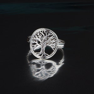 Könnte beinhalten: Ein silberner Ring mit einem Lebensbaum-Design. Der Ring liegt auf einem schwarzen Hintergrund.