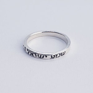 May include: A silver ring with Hebrew text inscribed around the band.