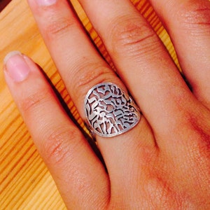 K&ouml;nnte beinhalten: Ein silberner Ring mit einem runden Design mit filigranen Ausschnitten. Der Ring wird an einem Finger getragen.