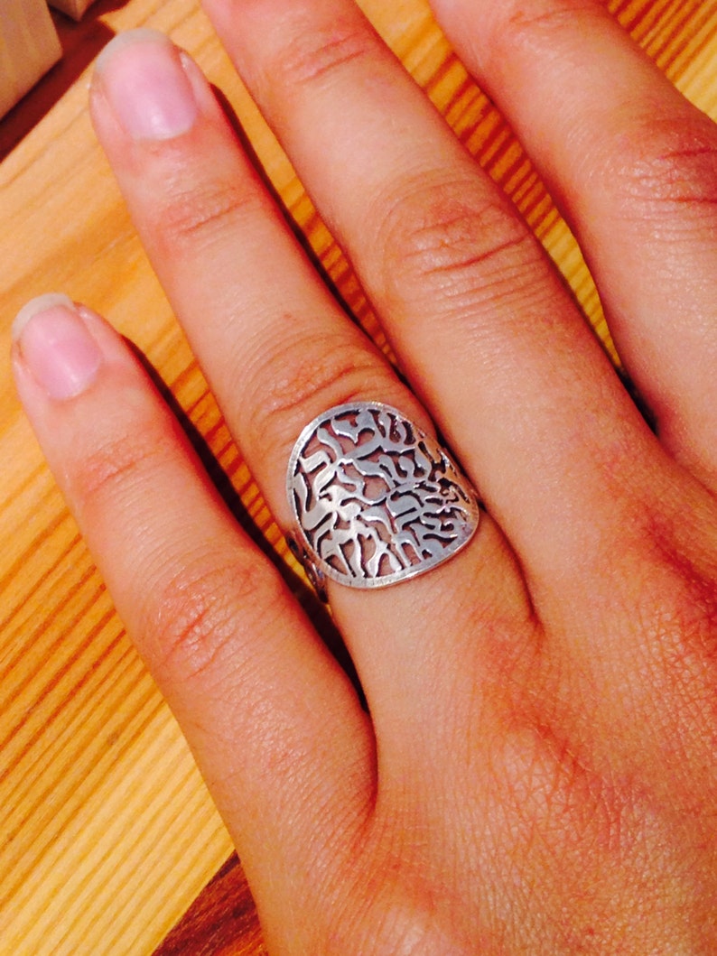 K&ouml;nnte beinhalten: Ein silberner Ring mit einem runden Design mit filigranen Ausschnitten. Der Ring wird an einem Finger getragen.