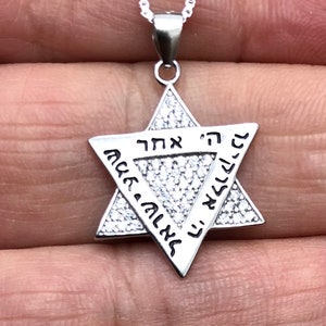 Könnte beinhalten: Eine silberne Davidstern-Halskette mit einer hebräischen Inschrift und klaren Zirkonia-Steinen.