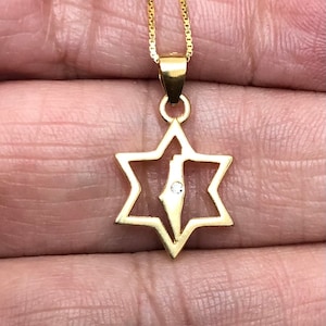 May include: A gold chain necklace with a pendant featuring a Star of David with a diamond-shaped outline of the country of Israel inside.
