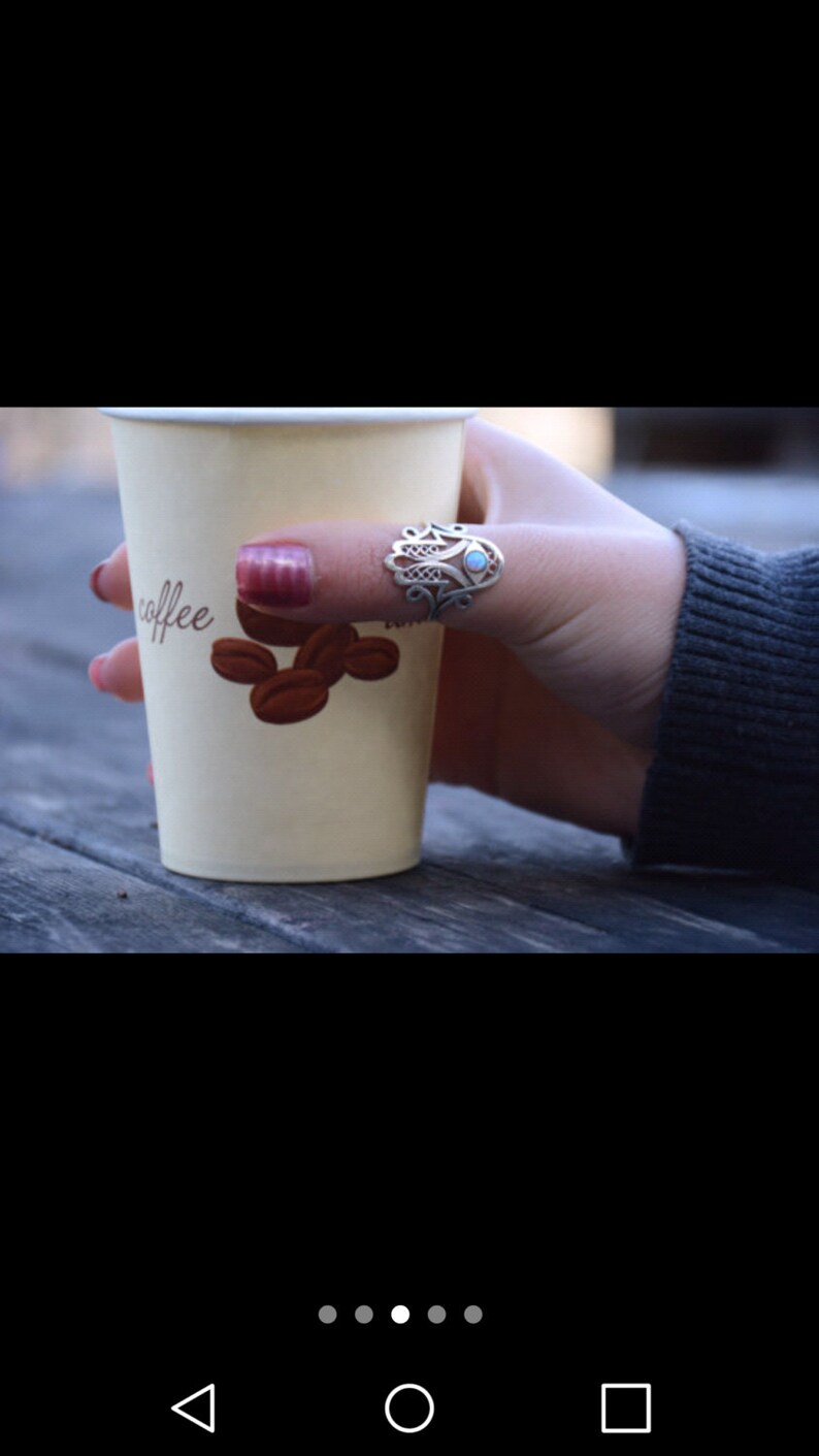 K&ouml;nnte beinhalten: Ein wei&szlig;er Pappbecher mit dem Wort "coffee" darauf. Der Becher wird von einer Hand gehalten, die einen silbernen Ring mit einem blauen Stein tr&auml;gt. Der Ring ist ein Hamsa-Hand-Design.