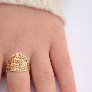 May include: A gold ring with a filigree design. The ring is on a finger.