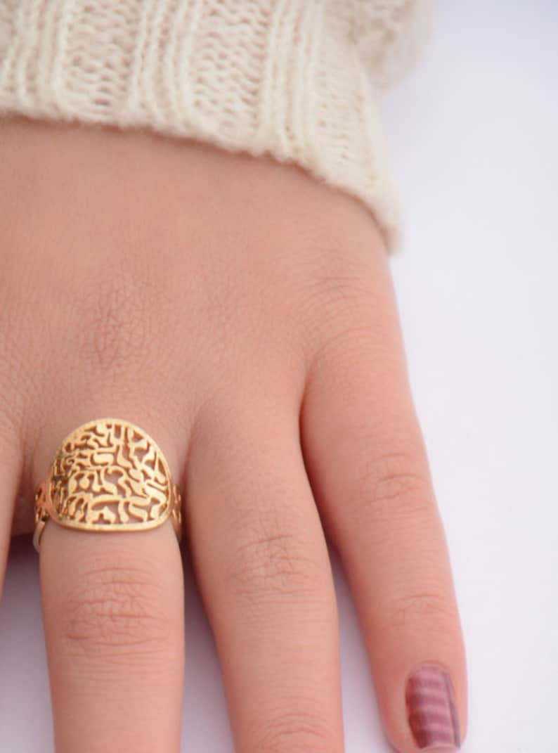 May include: A gold ring with a filigree design. The ring is on a finger.