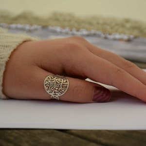 May include: A silver ring with a circular design featuring intricate cutouts. The ring is worn on a finger with a burgundy nail polish.