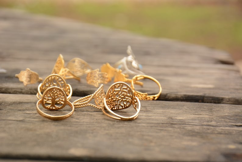 May include: A collection of gold-toned rings with intricate designs, including a tree of life motif, on a wooden surface.